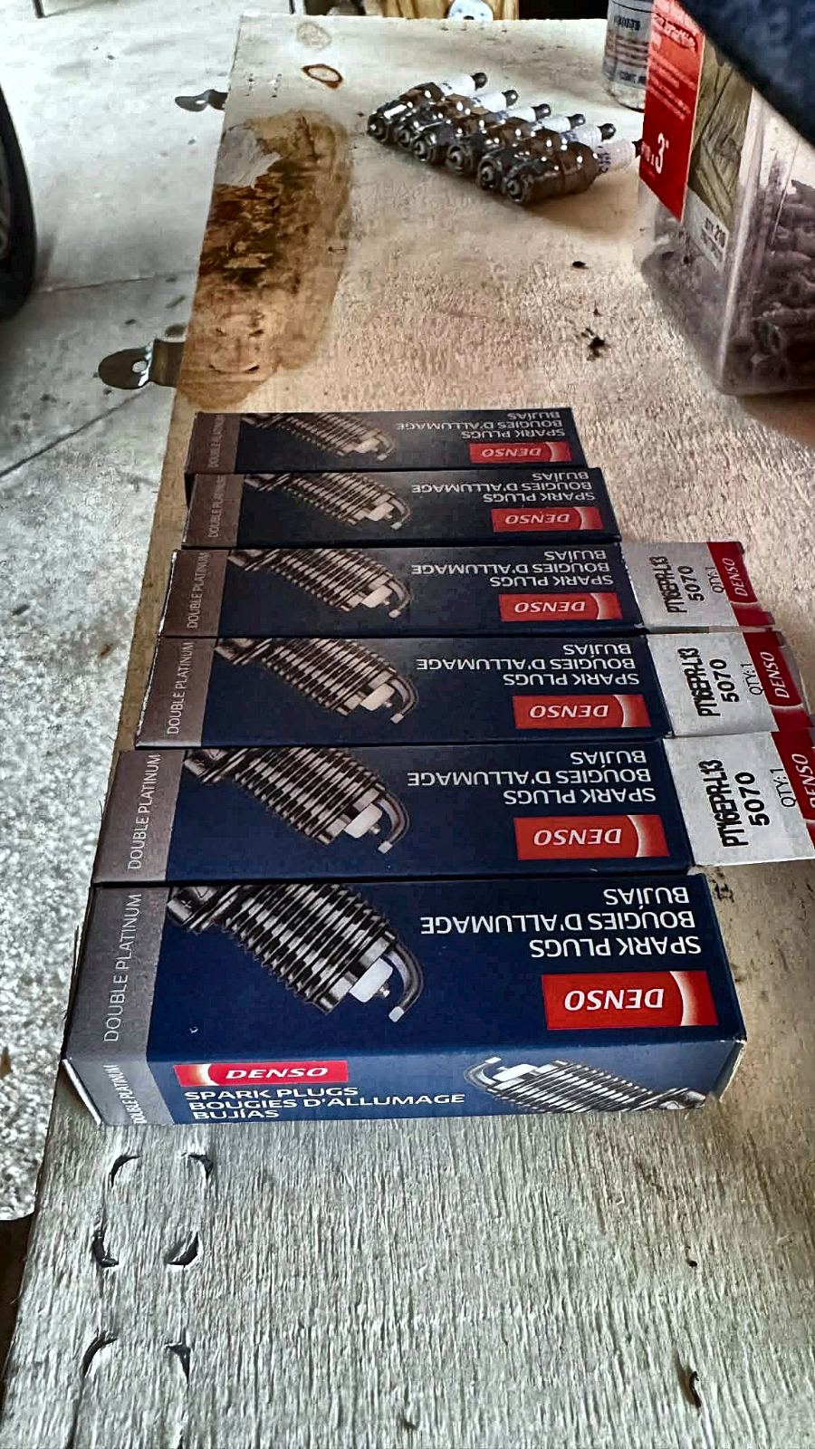 Six new Denso double-platinum spark plugs beside the old set